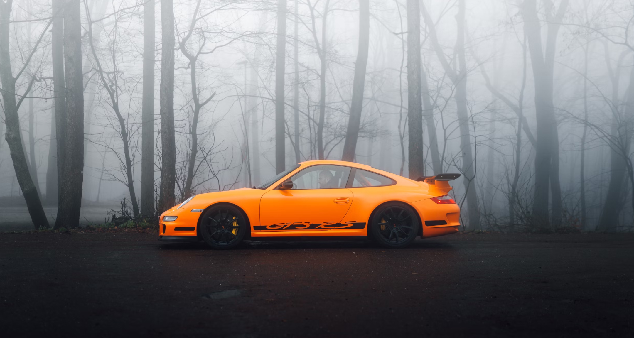 Image of an orange sports car parked in the middle of the forest.