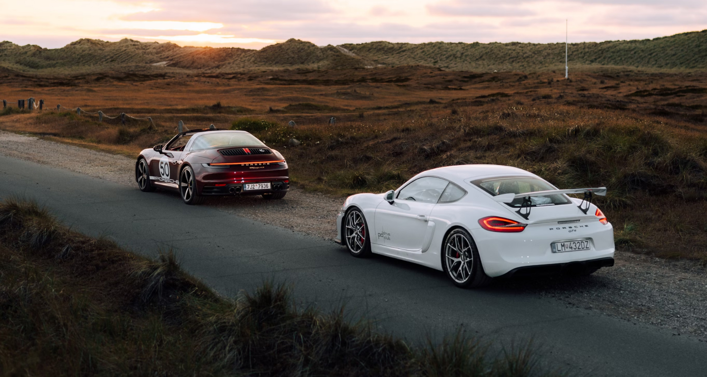 Image of two cars at sunset, one a Porsche Carrera and the other a Porsche, one behind the other.