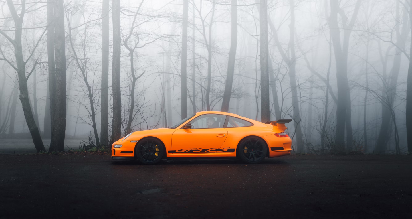 Image of an orange sports car parked in the middle of the forest.