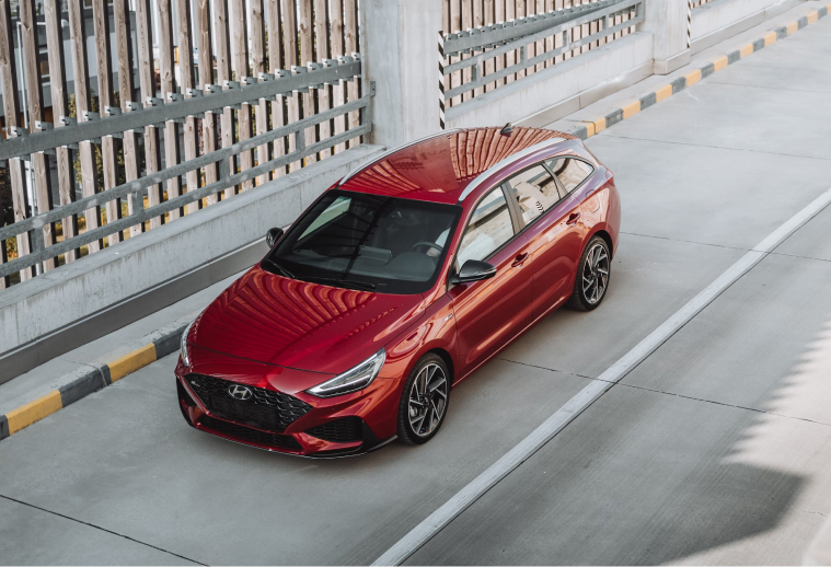 Image taken from above of a red car passing through the circular tunnel of a parking lot.